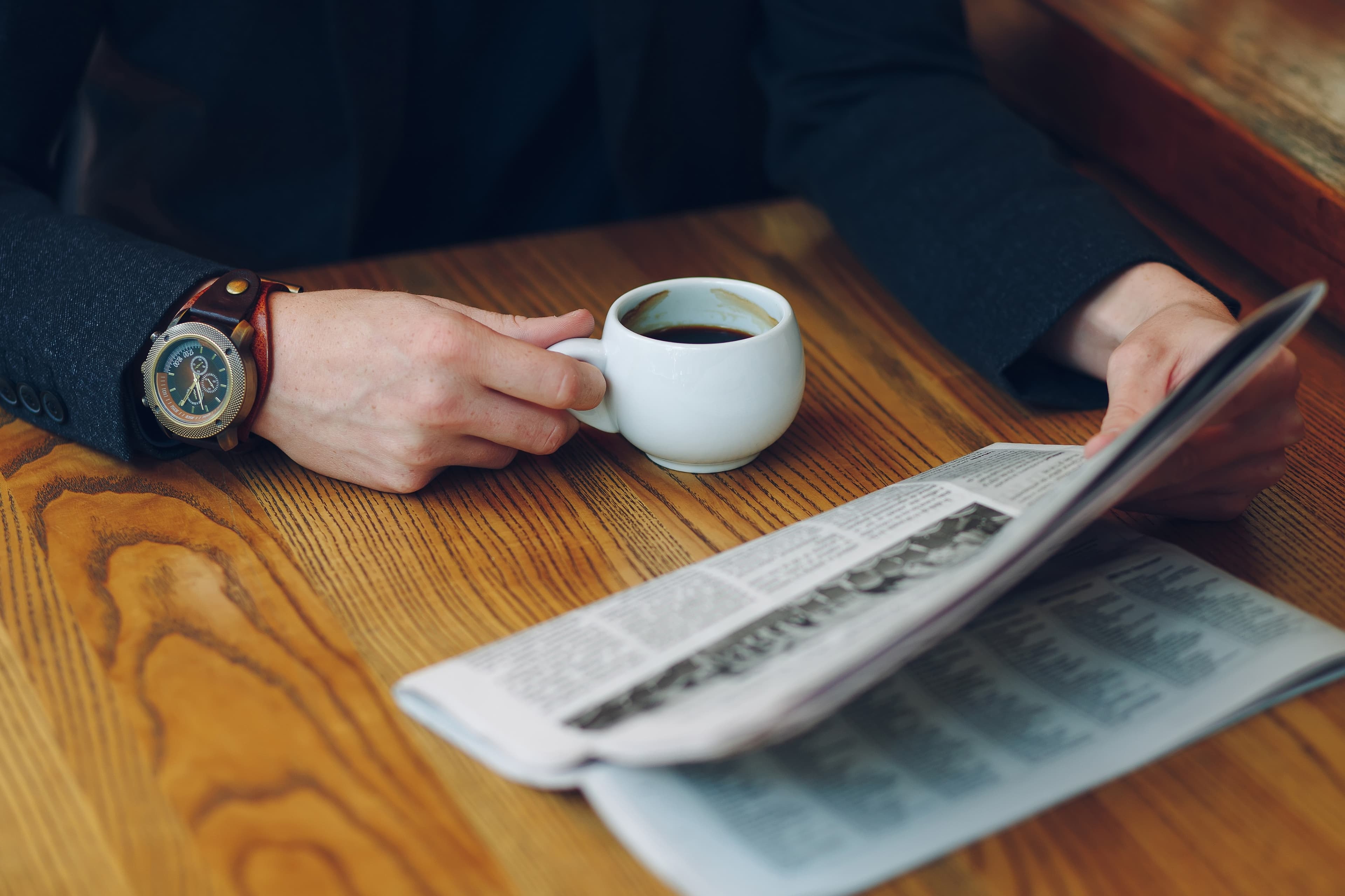 Person liest Zeitung und trinkt Kaffee – Moment der Information und Reflexion über das aktuelle Tagesgeschehen.