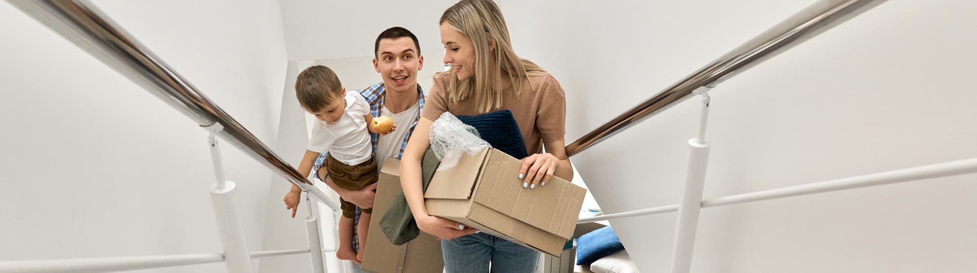 Eine glückliche Familie trägt beim Auslandsumzug voller Vorfreude Umzugskartons in ihr neues Zuhause mit Unterstützung von DACHSER & KOLB.