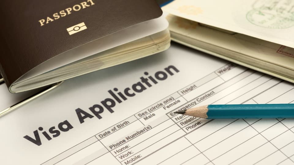 Ein englisches Visum-Antragsformular mit einem Reisepass und Stift zur Vorbereitung wichtiger Visa- und Aufenthaltsunterlagen für den Auslandsumzug mit DACHSER & KOLB.