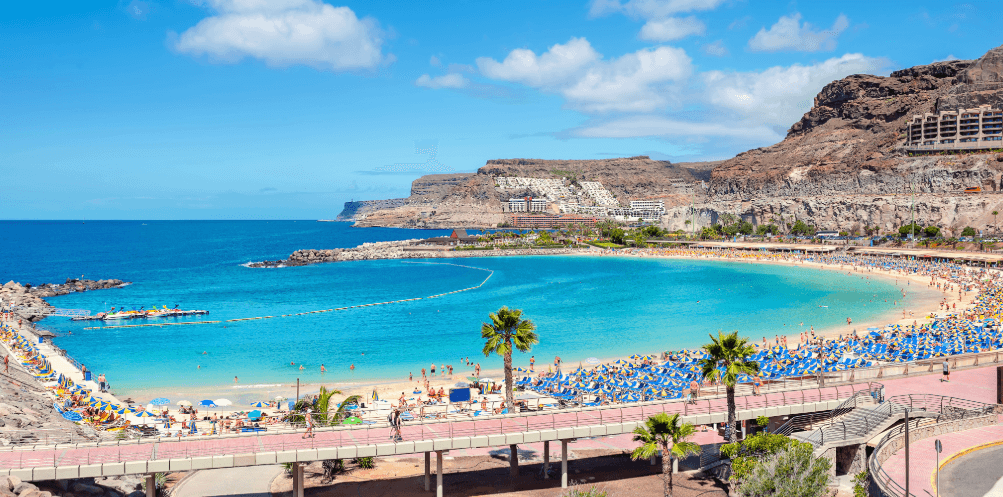 Bucht in Spanien mit Sandstrand, Palmen, türkisblauem Meer und felsiger Küstenlandschaft
