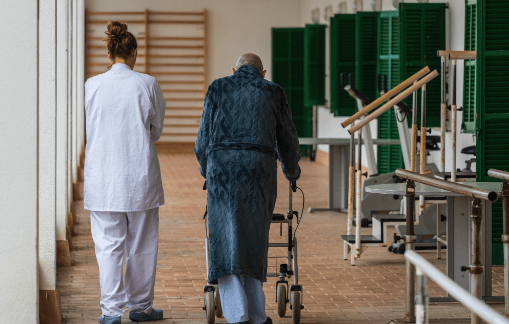 Pflegekraft begleitet ältere Person mit Rollator in einer medizinischen Einrichtung in Spanien