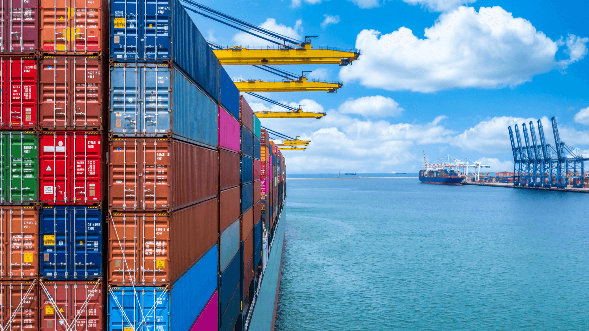Ein großes Containerschiff beladen mit farbigen Containern verschiedener Größen im Hafen unter blauem Himmel.