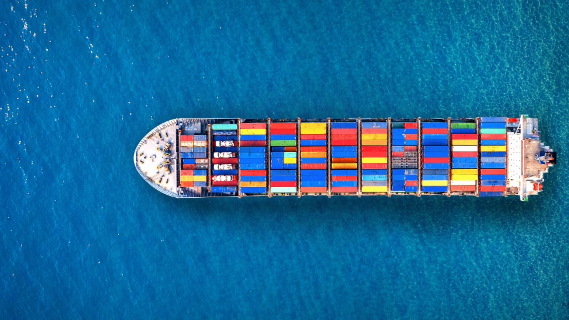 Luftaufnahme eines großen Containerschiffs beladen mit bunten Frachtcontainern auf offener See.