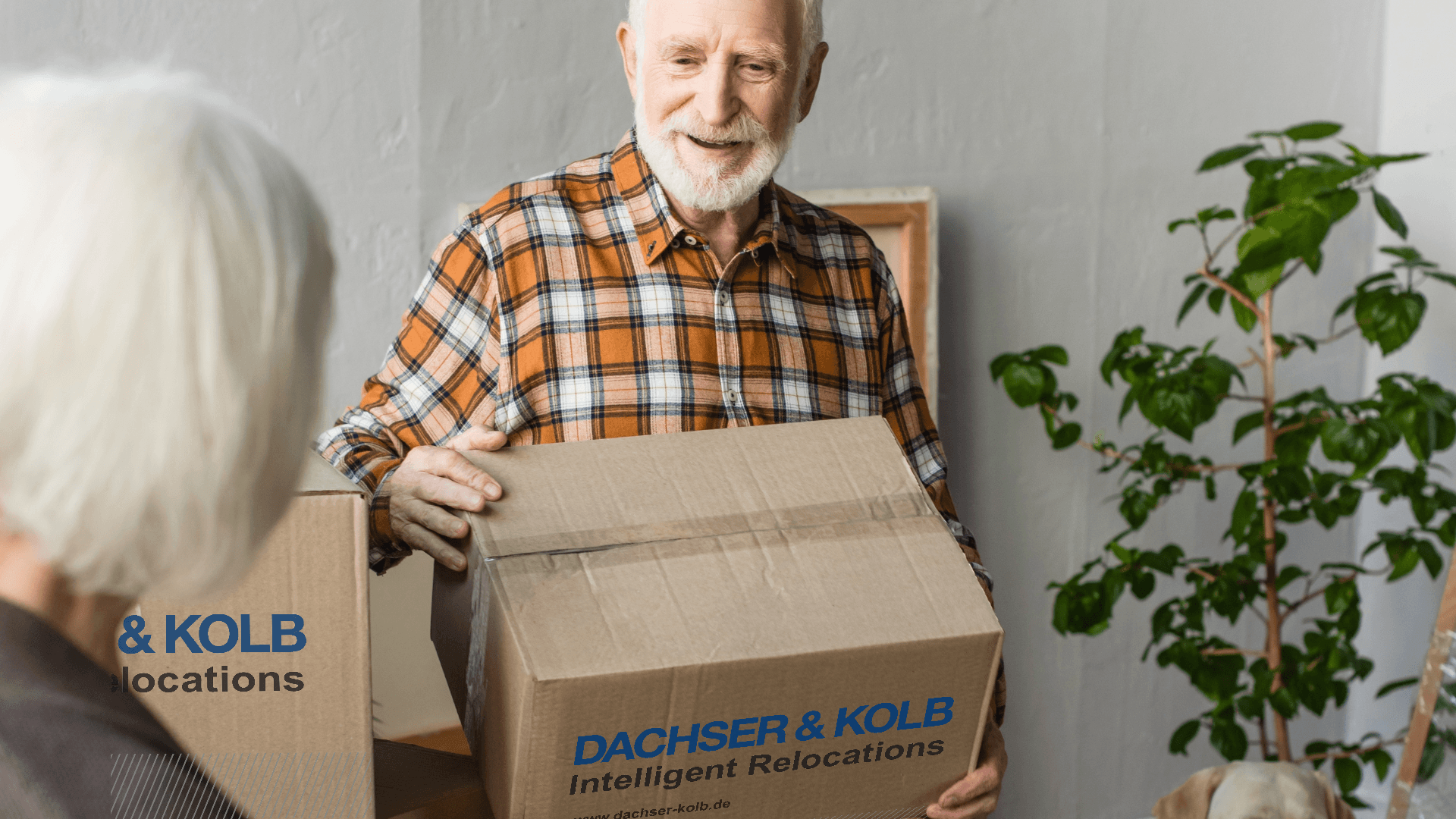 Senior trägt Umzugskarton mit DACHSER & KOLB – sicherer Seniorenumzug in gehobene Wohnresidenzen