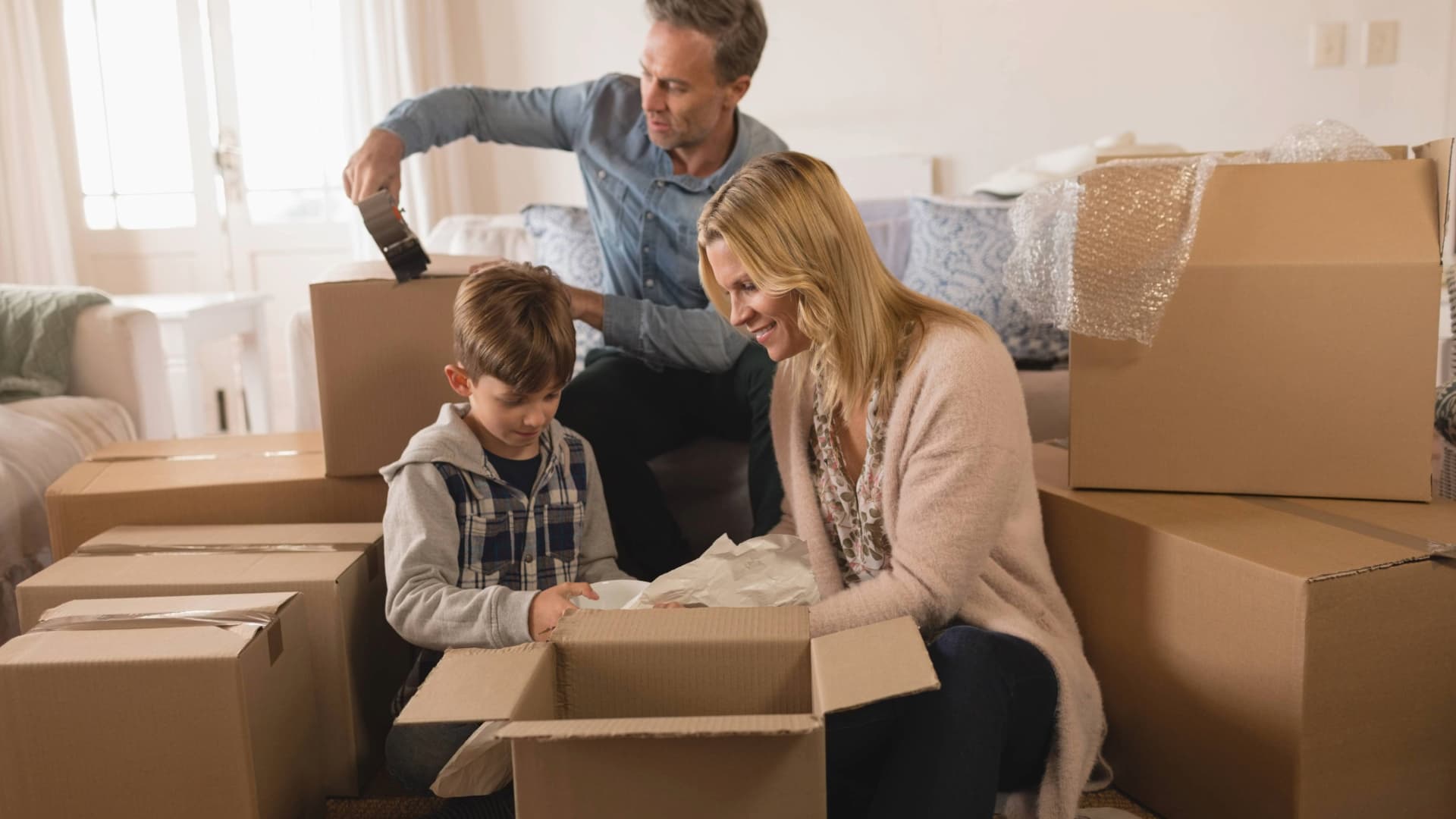 Eine Familie packt Umzugskartons in ihrem Zuhause aus oder ein. Kinder helfen beim "Packed by Owner" (PBO) Umzug.