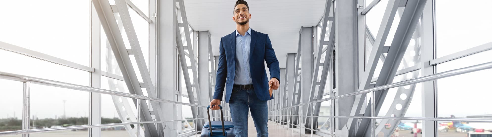 Ein lächelnder Expat im Business-Outfit zieht seinen Rollkoffer durch ein modernes Flughafenterminal zu einem internationalen Auslandseinsatz.