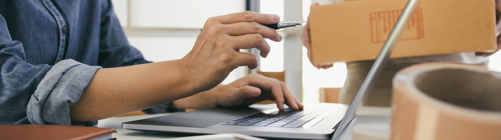 Eine Koordination am Laptop neben einem Umzugskarton und Paketband für die strategische Beschaffung von Moving- und Relocation-Leistungen im B2B-Procurement.