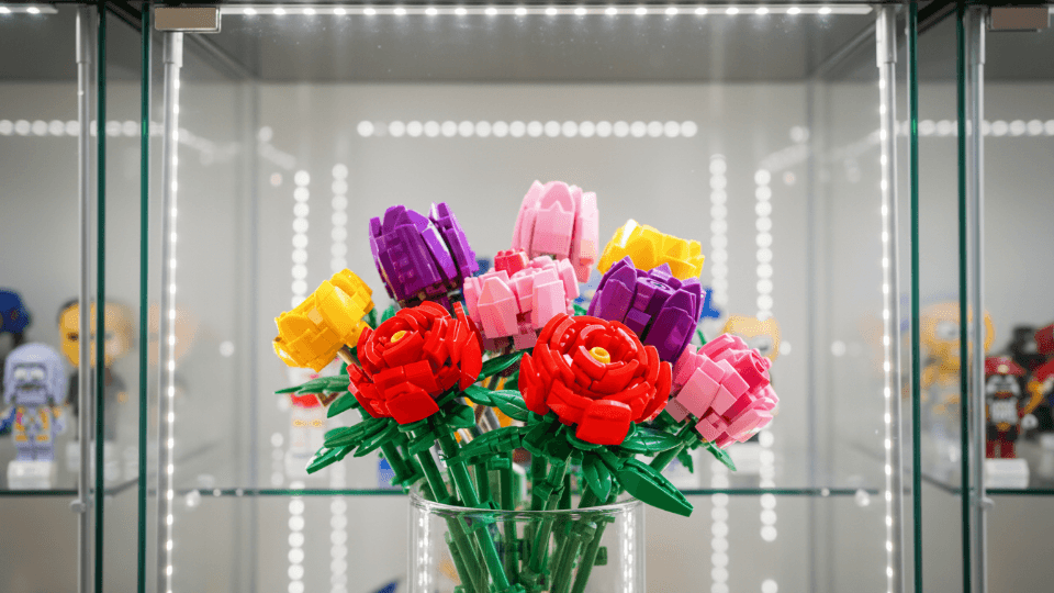 Ein bunter Klemmbaustein-Blumenstrauß in einer beleuchteten Glasvitrine mit Sammelfiguren vor der Transportsicherung durch DACHSER & KOLB.