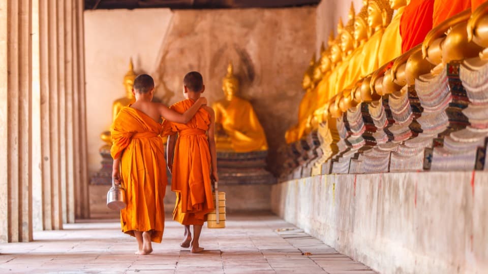 Zwei buddistische Möche laufen Arm in Arm durch einen Tempel in Thailand