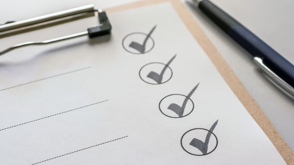 Eine strukturierte Checkliste mit gesetzten Haken auf einem Klemmbrett neben einem Kugelschreiber für eine transparente Projektabwicklung durch DACHSER & KOLB.