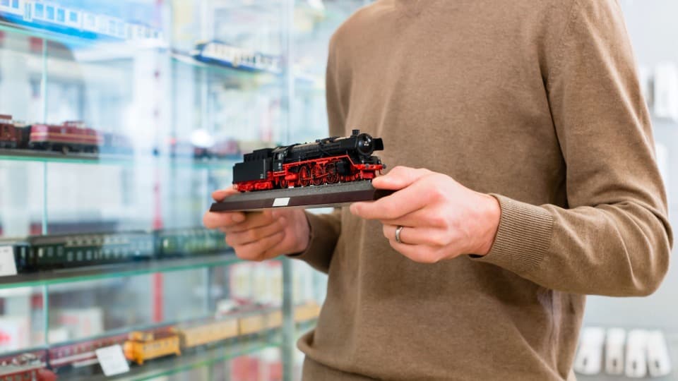 Ein Sammler nimmt vorsichtig eine Modelleisenbahn-Dampflokomotive aus einer Glasvitrine, um das Rollmaterial für den Umzug mit DACHSER & KOLB zu verpacken.