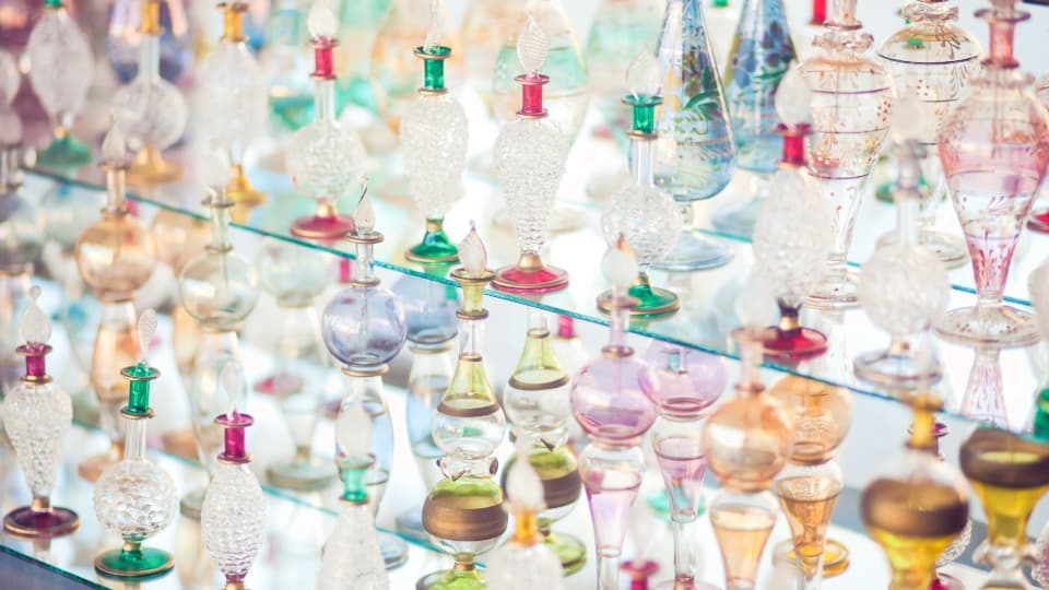 Eine Sammlung filigraner, bunter Glasflakons für Parfum auf Glasregalen vor dem sicheren Verpacken und Transport durch DACHSER & KOLB.
