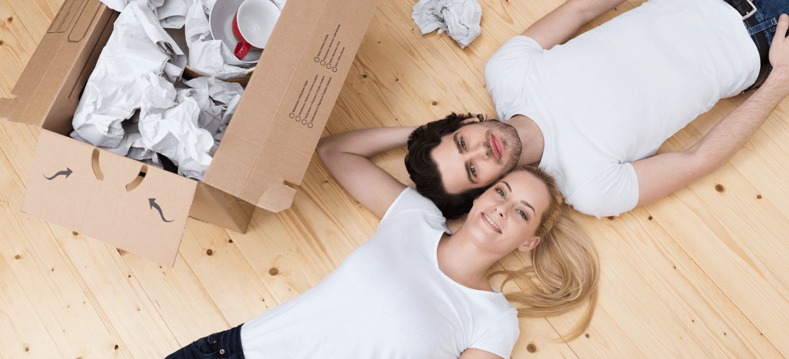 Glückliches Paar liegt entspannt neben ausgepacktem Karton. Prioritäten beim Umzug: Wichtiges zuerst auspacken, Zeit nehmen.