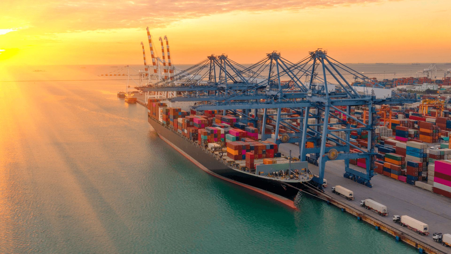 Beladenes Containerschiff einer Reederei am Kai im großen Hafen mit Kranen bei Sonnenuntergang.