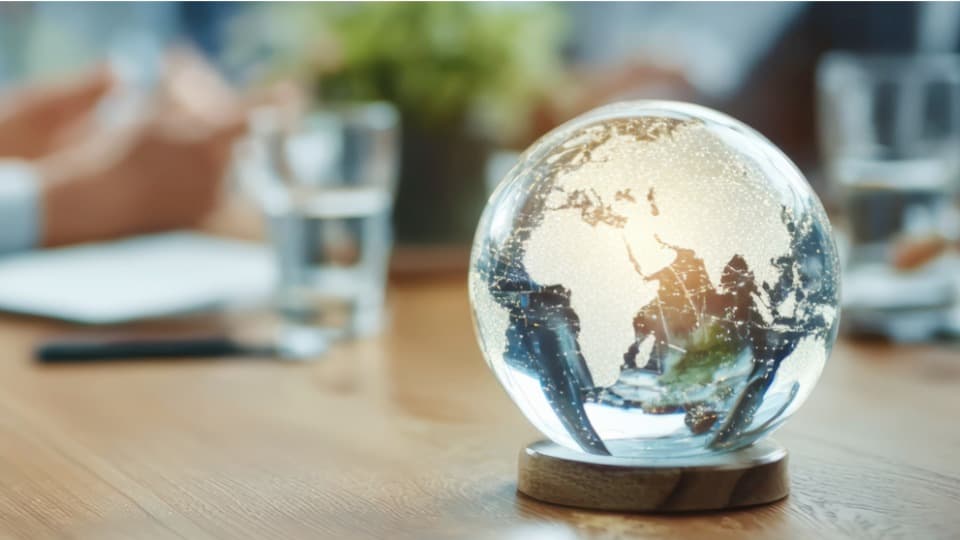 Ein von innen beleuchteter Glasklobus auf einem Besprechungstisch symbolisiert das globale Netzwerk von DACHSER & KOLB für die weltweite Wohnungssuche und Relocation von Expats.