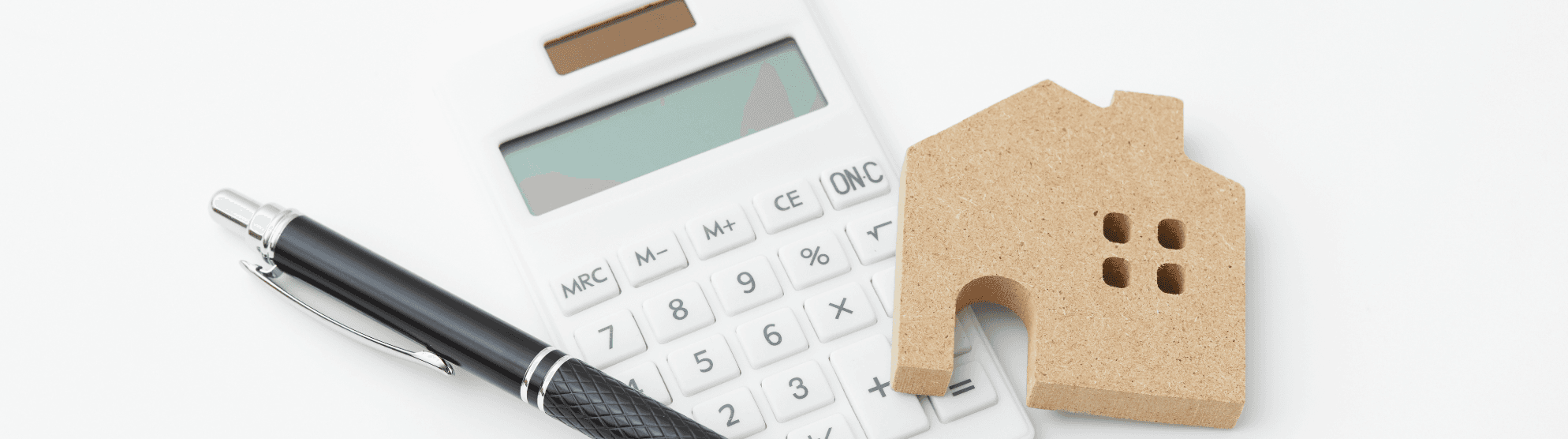 Taschenrechner, Stift und Holzhaus – Symbole für finanzielle Planung und Tipps zur Berechnung von Umzugskosten.
