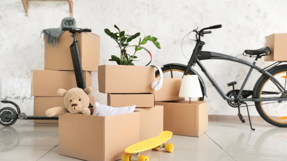 Gepackte Umzugskartons mit einem Fahrrad und Zubehör bei der Planung, was Kunden selbst mitnehmen und was DACHSER & KOLB transportiert.