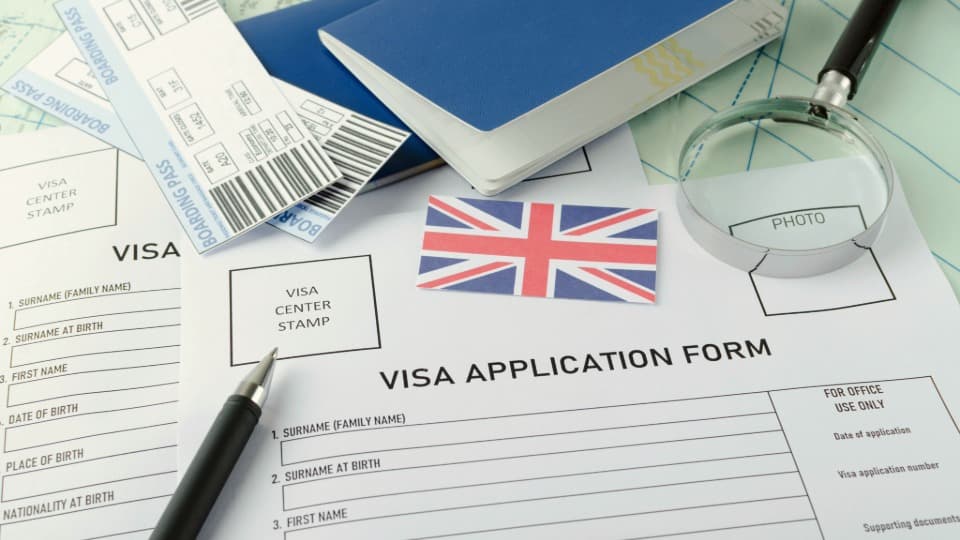 Formulare für UK-Visumantrag mit Reisepass, Boardingpässen und Lupe auf einem Schreibtisch