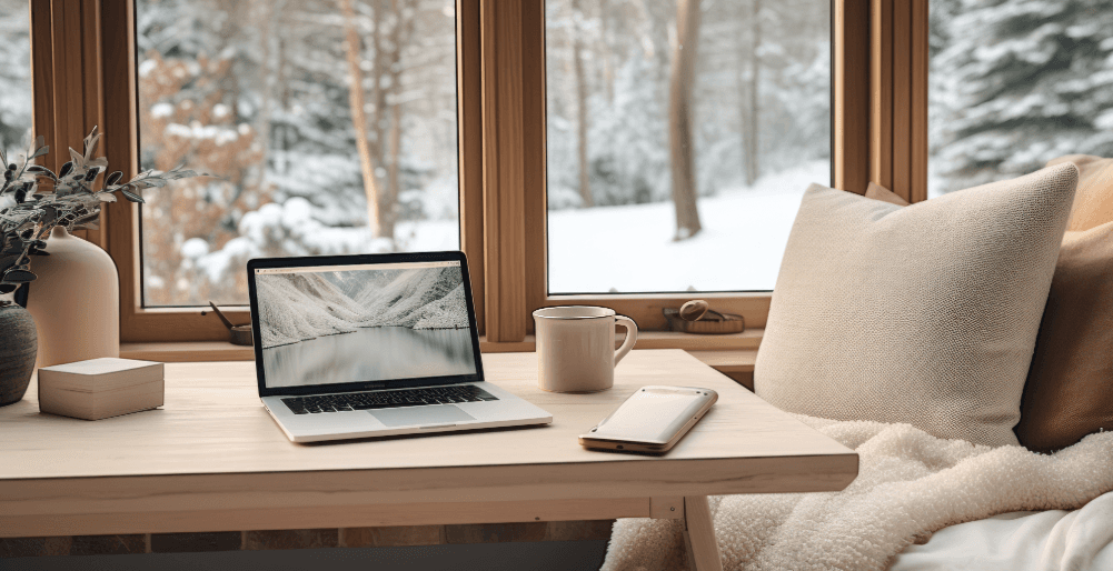 Cozy home office after winter move with laptop, hot drink and snowy forest view through the window