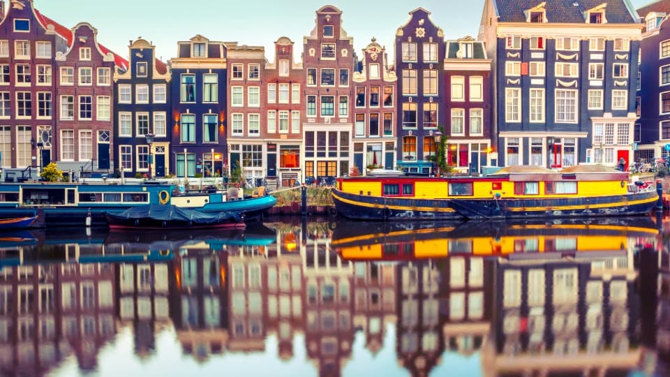 Grachtenhäuser und Hausboote an einem Kanal in Amsterdam mit Spiegelung im Wasser
