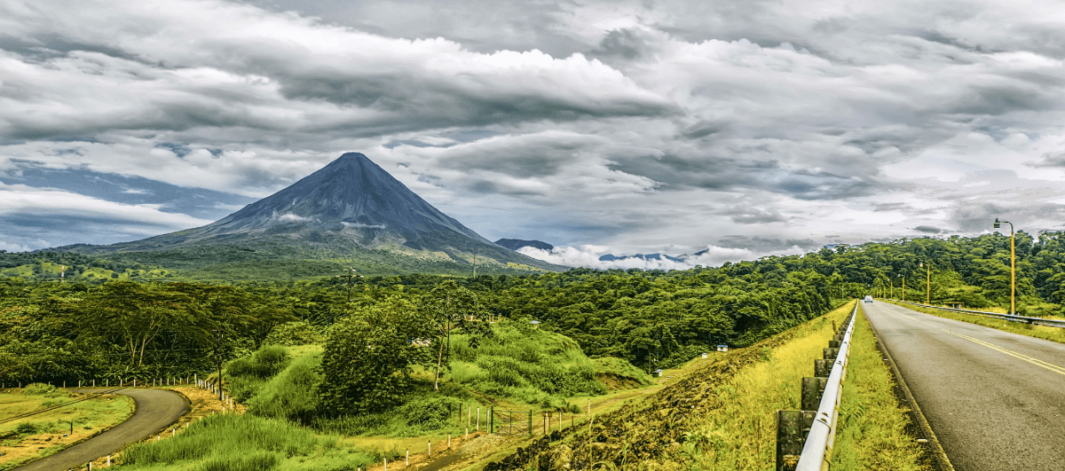 Vulkan in Costa Rica mit Straße, Regenwald und bewölktem Himmel