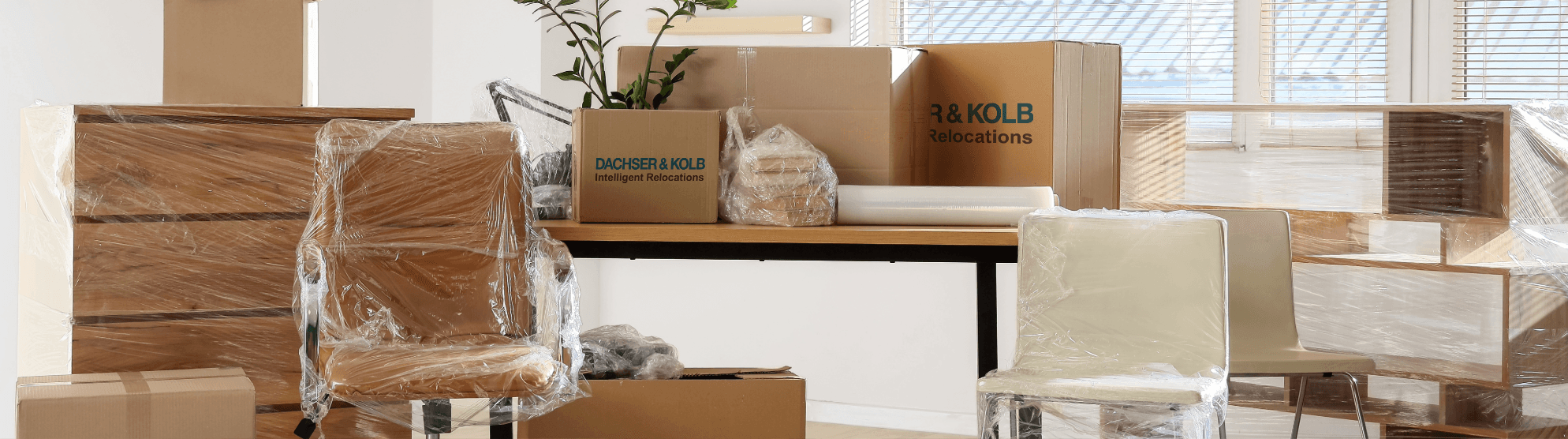 Verpackte Büromöbel und Umzugskartons mit DACHSER & KOLB Emballage in hellem Büro vor dem Firmenumzug