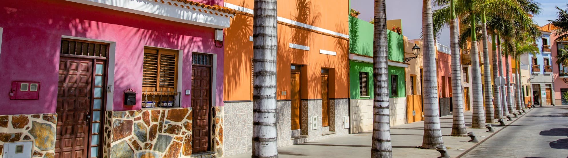 Colorful pink and orange house fronts along a palm-lined street in Tenerife, serving as a featured image for shipping moving boxes with DACHSER & KOLB.