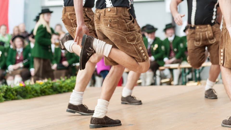 Kultur in Österreich - Schuhplattler tanzen auf einer Bühne, im Hintergrund ist eine Musikkapelle zu sehen