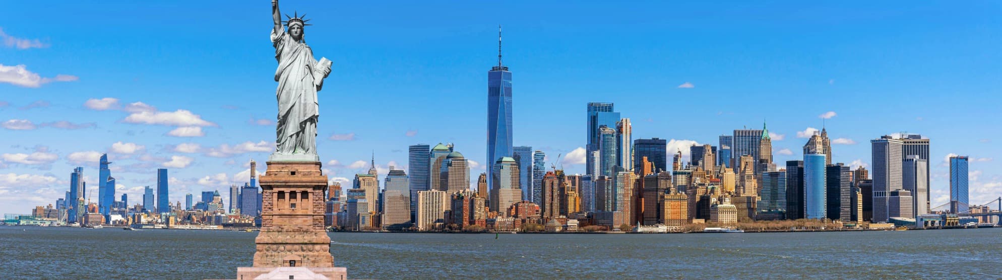Auswandern nach USA – Freiheitsstatue vor Skyline von New York City bei blauem Himmel