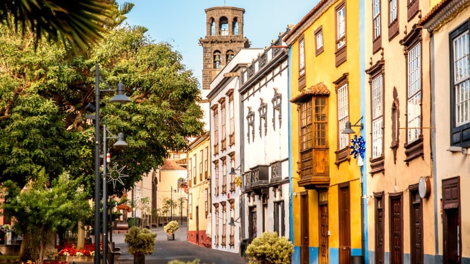 Historic street with colorful colonial houses and the church tower of Iglesia de la Concepción in La Laguna, Tenerife, representing moving box transport services by DACHSER & KOLB.