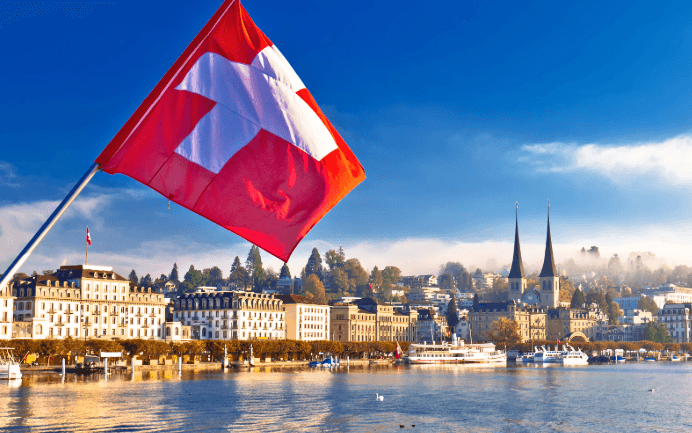 Schweizer Flagge am See mit Stadtansicht – Symbolbild für einen Umzug von Deutschland in die Schweiz