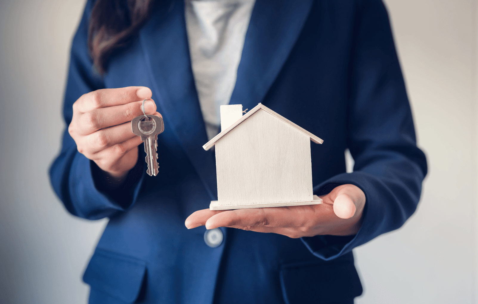 Person hands over key and model house – symbolic image of apartment handover or real estate transfer