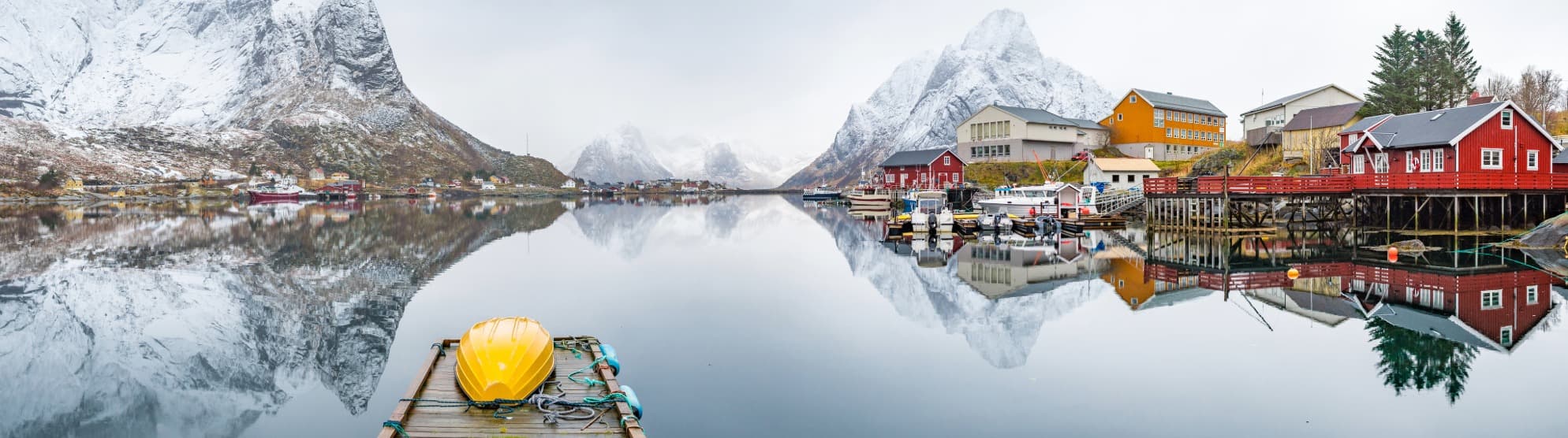 Fjorddorf in Norwegen mit schneebedeckten Bergen und Spiegelung im ruhigen Wasser